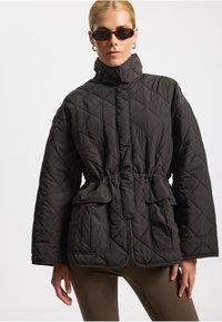 Gequilted zwarte jas met hoge kraag, getailleerde taille en twee voorzakken. Kenmerkt een gestructureerde stof met diamanten patroon en een losse pasvorm.