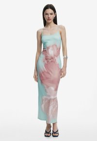 Rochie maxi din satin de culoare verde mentă cu un model abstract de flori roz. Dispune de bretele subțiri și o siluetă ajustată, asortată cu pantofi cu toc navy.