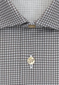 Overhemd met knopen, met een wit-bruine geometrische print, voorzien van een puntige kraag en een enkele crèmekleurige knoop bij de nek.