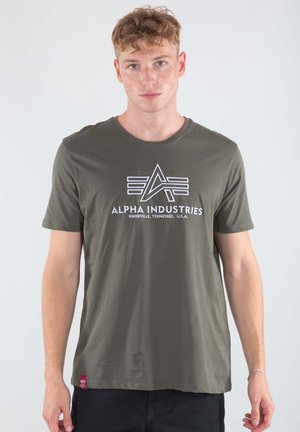 Olive green cotton t-shirt featuring a white logo with geometric design and text. Short sleeves and round neckline, tag visible at hem.