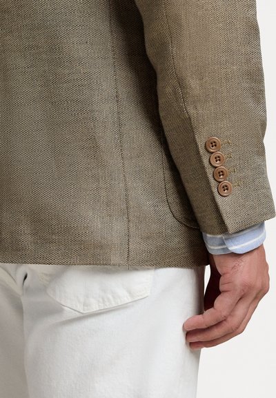 Beige tkaný blazer s texturovanou látkou, čtyřmi hnědými knoflíky na manžetách a světle modrou a bílou pruhovanou košili viditelnou pod ním.