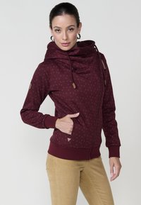 Bordo hooded dukserica s patentnim zatvaračem, s preklopom na vratu, teksturiranim uzorkom, vezicama i bočnim džepovima; sadrži kožne detalje na rukavima.