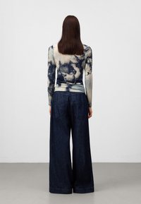 Langarmtop met een blauw en crèmekleurig tie-dye patroon, gecombineerd met wijde, donkere denim jeans met twee achterzakken.