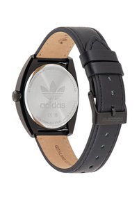 Montre ronde noire avec un dos en acier inoxydable, bracelet en cuir et doublure intérieure texturée. Présente le logo Adidas et une boucle réglable.