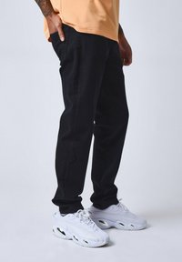 Jeans negros de corte ajustado, exhibidos junto a zapatillas blancas. Los jeans presentan un diseño clásico de cinco bolsillos y una textura suave.