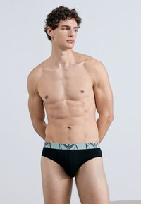 Cuecas pretas com uma cintura elástica azul clara apresentando um padrão de logotipo. O tecido parece liso com um design ajustado.