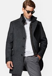 Szary tweedowy płaszcz z dobrze zarysowanym kołnierzem, trzema guzikami i pikowaną podszewką. Nosi się go na szarym golfie, w zestawieniu z szarymi spodniami.