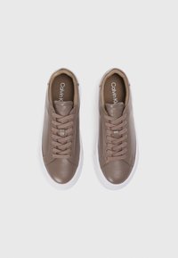 Καφέ δερμάτινα sneakers με λευκές καουτσούκ σόλες, στρογγυλή μύτη και επίπεδες κορδόνες. Ορατό λογότυπο "Calvin Klein" στην εσωτερική σόλα.