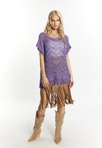 Vestido poncho de punto abierto en color púrpura con un patrón en zigzag y flecos de ante color caramelo en el dobladillo, combinado con botas de cowboy de tacón alto en color caramelo.