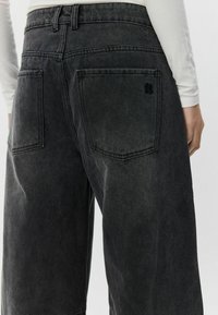 Črne široke kavbojke iz denima z zbledelim videzom, ki imajo dva zadnja žepa in majhen logotip nad enim žepom.