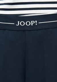 Σκούρα μπλε μέση με λευκό λογότυπο "JOOP!" πάνω από μονόχρωμο σκούρο μπλε ύφασμα και στρώση οριζόντιων ριγών σε μαύρο και λευκό.