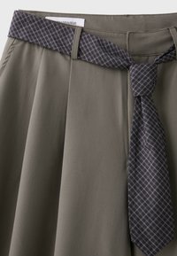 Jupe vert olive avec plis et ceinture en tissu à carreaux gris foncé nouée en nœud à la taille.