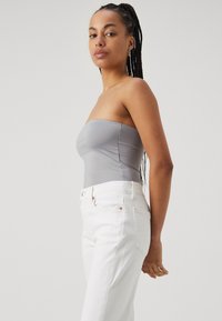 Top gris sin tirantes de material suave, combinado con jeanes blancos de tiro alto. Los jeanes presentan remaches sutiles de cobre y costuras clásicas.