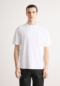Hvit bomullen T-skjorte med avslappet passform, kortermet og rund hals, satt sammen med mørk denimjeans. Enkelt design, ingen mønstre eller dekorasjoner.