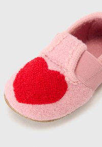 Pink felt slipper with a large fuzzy red heart applique, elastic strap, and beige rubber sole. Soft texture; rounded shape.