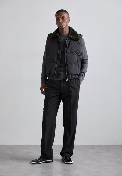 Črna napihnjena jopica z zelenim krznenim ovratnikom, nosi se nad sivo majico. Ozkih črnih hlačah in črnih čevljih z belimi podrobnostmi. Nevtralna ozadje.