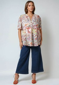 Floral blouse with short sleeves in pastel colors, featuring a split neckline. Paired with wide-leg dark blue denim pants and orange strappy heels.
