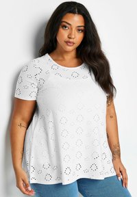 Top blanco de manga corta con escote redondeado, que presenta bordados con patrones recortados y una forma relajada y acampanada.