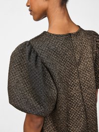 Mulher vestindo um vestido texturizado, cintilante em preto e dourado, com mangas curtas e bufantes, mostrado de costas e de lado.