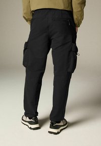 Pantaloni cargo negri, realizați dintr-un material durabil, cu buzunare laterale, talie elastică și picioare conice, asortați cu sneakers gri și negri.