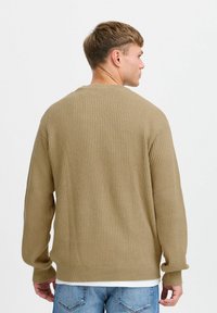 Beige ribbed sweater with a crew neckline and long sleeves. The texture is knitted, featuring a relaxed fit and slightly dropped shoulders.