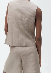 Beige gestreifter ärmelloser Oberteil mit lockerer Passform, kombiniert mit passenden beigen Shorts. Glatte Textur und dezente vertikale Linien.