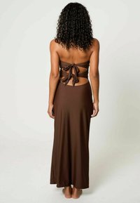 Brun maxiklänning med en strapless design. Har en knytning på baksidan och utskärning, tillverkad av ett mjukt, lätt tyg.