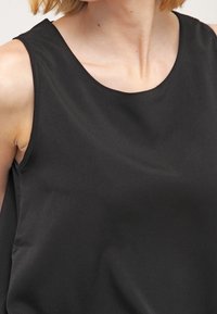 Top negro sin mangas con una textura suave, escote redondo y un sutil drapeado. El material parece blando y ligero.