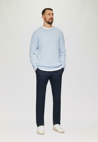 Lichtblauwe crew neck trui over een wit shirt, gecombineerd met donkerblauwe broek en witte sneakers. Eenvoudig ontwerp, casual stijl.