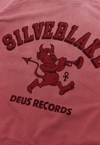 Red sweatshirt featuring a cartoon devil character playing a trumpet. Text reads "SILVERLAKE" and "DEUS RECORDS" in bold letters.