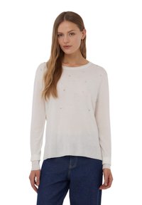 Pullover cremoso a maniche lunghe realizzato in tessuto leggero, con scollo rotondo e impreziosito da piccole pietre decorative distribuite in modo uniforme.
