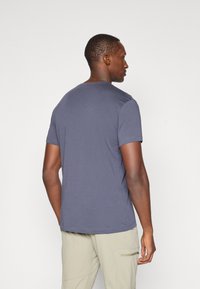 Jersey T-skjorte i mørkegrå, rund hals, kort erm. Myk tekstur, avslappet passform, vist på en modell sett fra bak, kombinert med lyse bukser.