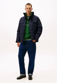 Granatowa puchowa kurtka z wysokim kołnierzem, zielona bluza z kapturem, koszula w paski, niebieskie dżinsy i czarne buty. Casualowa stylizacja z praktycznymi detalami.