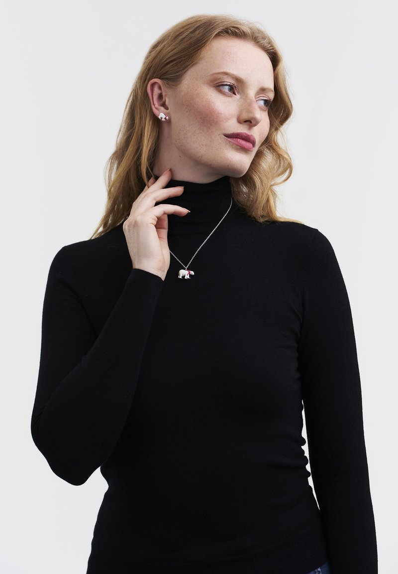 Jauna sieviete ar sarkaniem matiem, valkājot melnu augstu apkakli, pieskaras kaklam, rādot baltu lāča formālu piekariņu uz kaklarotas un atbilstošas lāča formas auskarus.