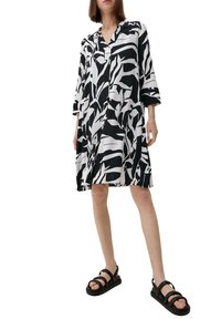 Schwarz-weißer Hemdkleid mit Blattmuster, Kragen, Dreiviertelärmeln und lässiger Passform, kombiniert mit schwarzen Riemchensandalen.