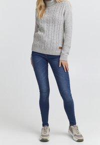 Gray knitted turtleneck sweater with cable details, paired with blue skinny jeans and gray sneakers featuring white and olive accents.