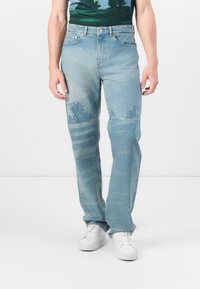 Světle modré džíny s rovnými nohavicemi, které mají jemně opotřebovaný vzhled a abstraktní krajinný potisk na přední straně.