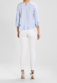 Lys blå stribet bluse med trekvartærmer, flæset kant og nøglehul detalje på ryggen, parret med hvide skinny jeans og sølvhæle.