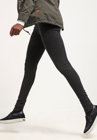 Černé skinny džíny s těsným střihem, mají hladkou texturu a klasický design s pěti kapsami. Nosí se s černými slip-on teniskami.