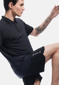 Sort kortærmet polo med krave og to-knaps placket. Sorte sportsshorts med "NO PAIN NO GAIN" trykt på siden.