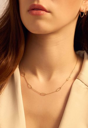Gouden ketting met ovale schakels, tentoongesteld tegen een neutrale achtergrond, met gladde, glanzende oppervlakken en een delicate vormgeving.