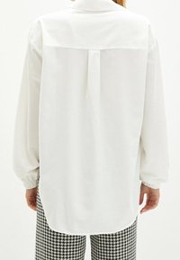Hvid langærmet bluse lavet af letvægtsstof, med rygskødet og samlede manchetter. Sammen med bukser i sort-hvid houndstooth mønster.
