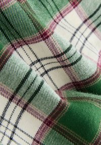 Grüner und elfenbeinfarbener Stoff mit lila und schwarzen Akzenten; weiche Textur, mit klassischem kariertem Muster und eingewebten Details.