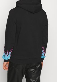 Sweatshirt à capuche noir avec des manches bleues, orné de motifs de flammes roses. Confectionné en matériau doux, il offre une coupe décontractée et un ourlet côtelé.
