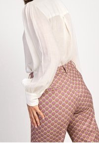 Ljus, genomskinlig vit blus med puffärmar som kombineras med figursydda, mönstrade byxor i rosa och lavendeltoner med geometriska motiv.