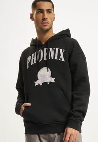 Svart hettegenser med lommer, med "PHOENIX" i hvite bokstaver og et rundt grafisk motiv med et banner under. Laget av mykt stoff.