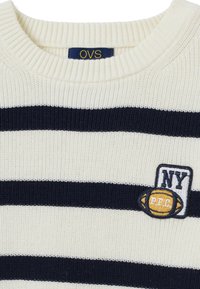 Creme- und marineblau gestreifter Strickpullover mit geripptem Rundhalsausschnitt, ausgestattet mit einem gestickten Patch mit "NY" und einem Football-Design.