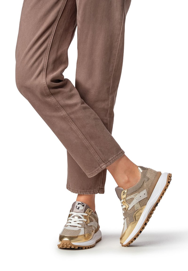 Baskets combinant des matériaux beige et doré, avec un design texturé, des lacets blancs et une semelle multi-texturée.