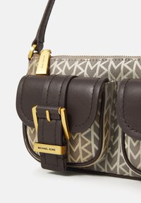 Brown leather crossbody bag with gold hardware and two front pockets. Features a tan patterned canvas, zipper closure, and logo detail.