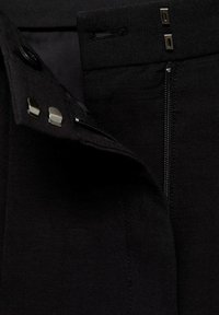Black structured pants featuring a smooth texture, a concealed zipper closure, and metal button accents at the waistband.
